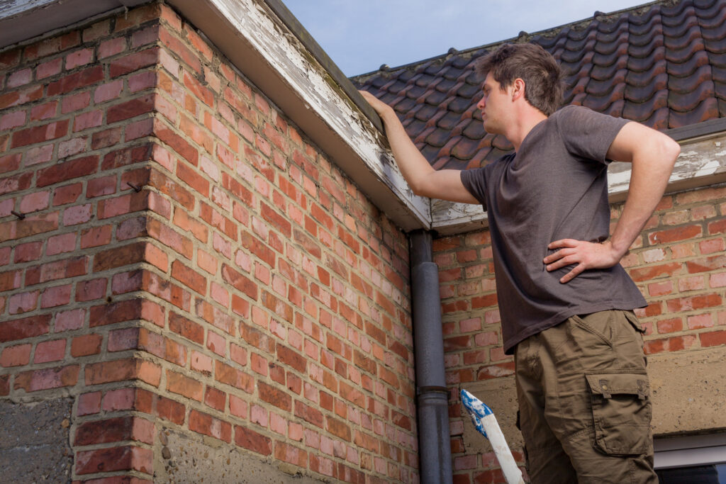 Young man inspecting the roof of an old house standing on a ladder